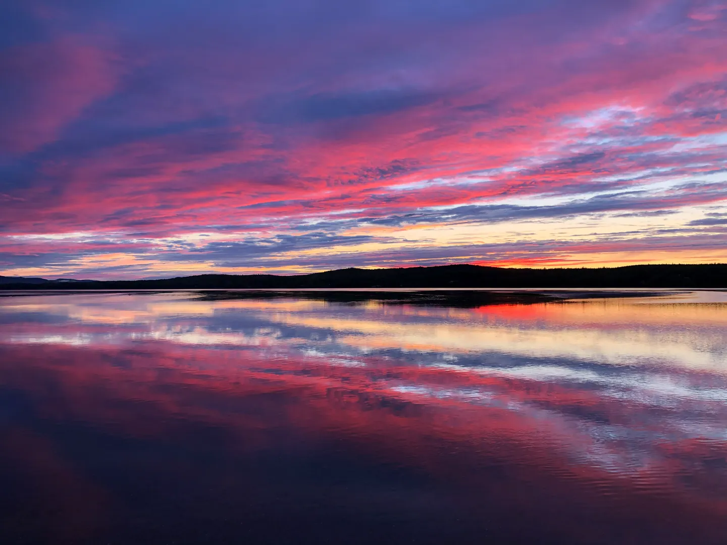 Ciel rose et mauve au crépuscule, reflété dans l’eau calme de la baie